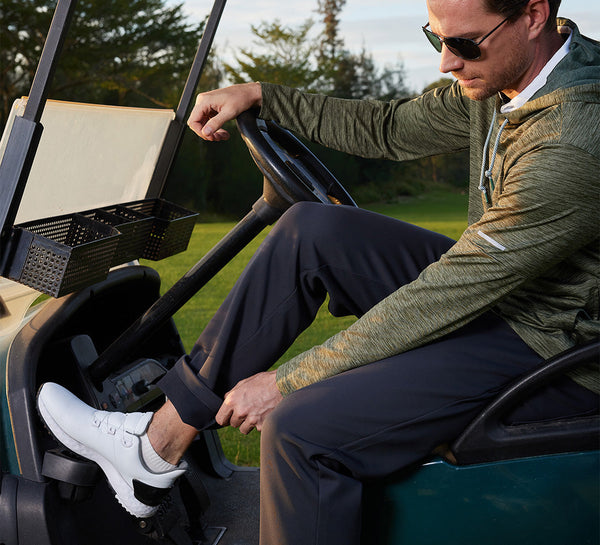 Model sitting in a golf cart, one hand on the wheel and the other showing the fleece-lined interior of the pants.