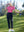 Model in rose women's performance solid polo holding a golf club outdoors