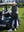 Model leaning on a golf cart, wearing black women's lightweight slim-fit puffer vest with one hand in pocket.
