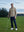 Model on grass under blue sky, leaning on golf club, wearing quarter zip melange pullover in brown melange.